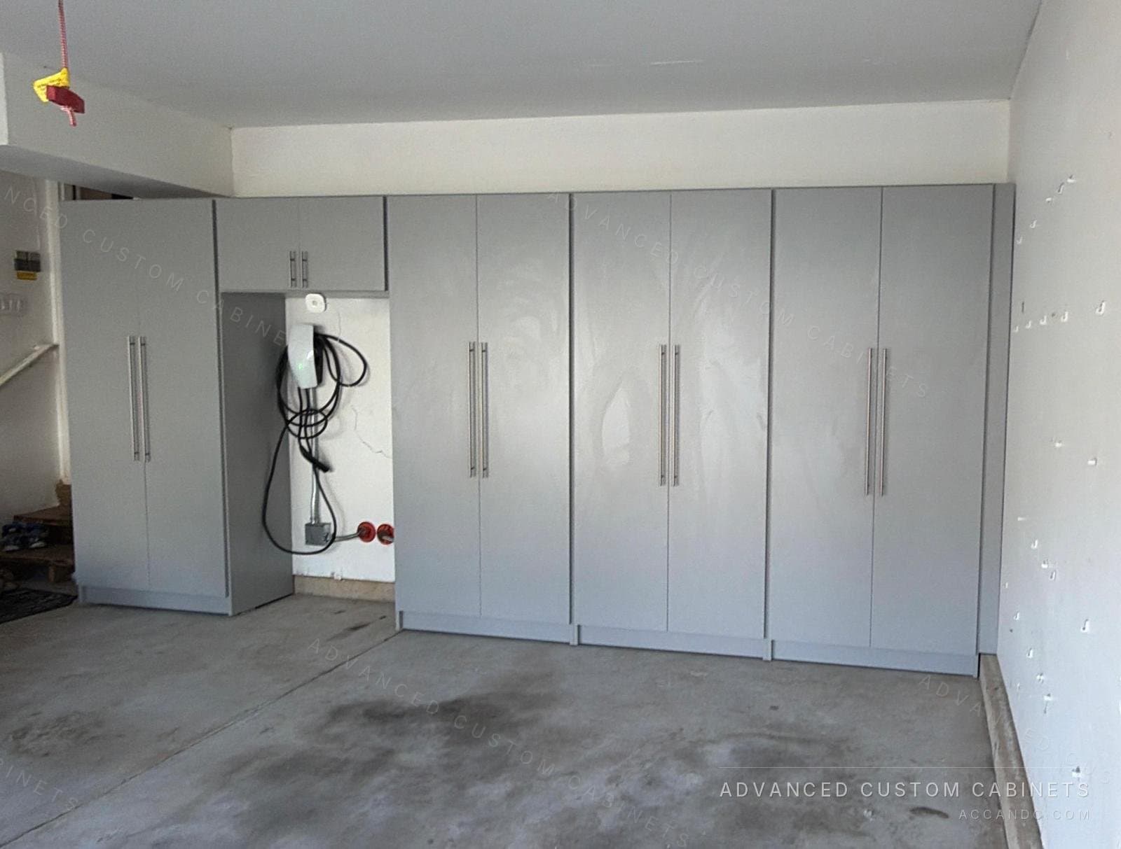 Custom gray garage storage wall with full-height double-door cabinets, long bar pulls, and an open niche for an EV charger