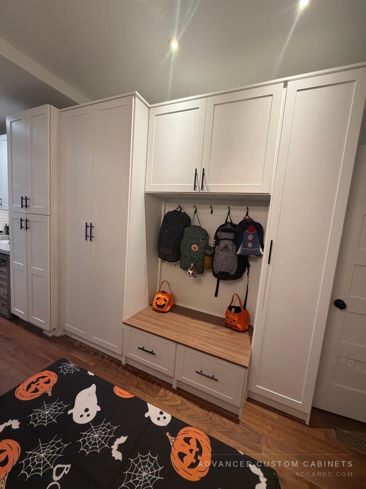 White shaker mudroom wall with tall pantry and coat cabinets, an upper cabinet over coat hooks and a wood-top storage bench with two drawers