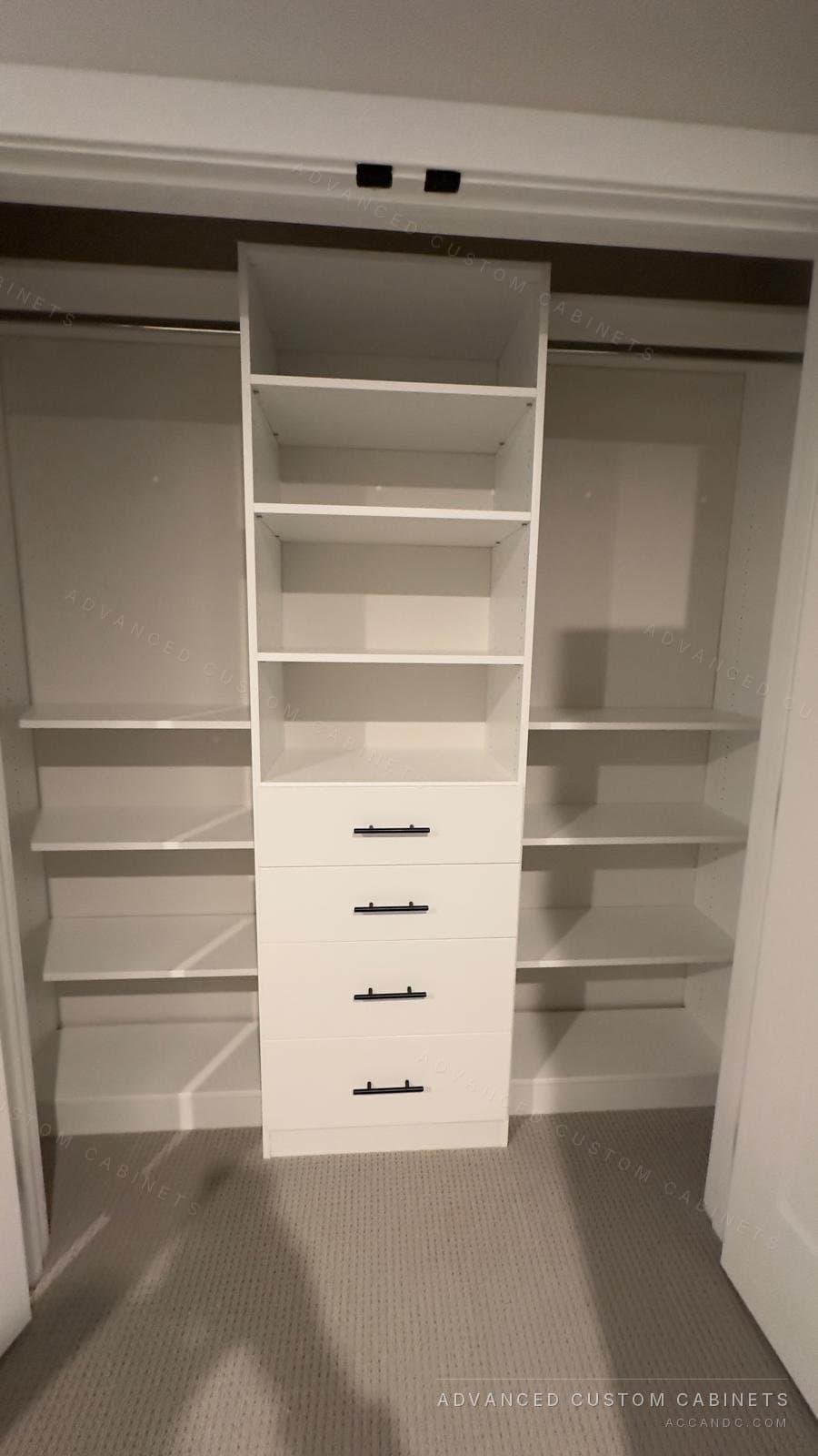 Wide white reach-in closet with a center tower of open shelves over four drawers with black bar pulls and hanging sections with shelves on both sides