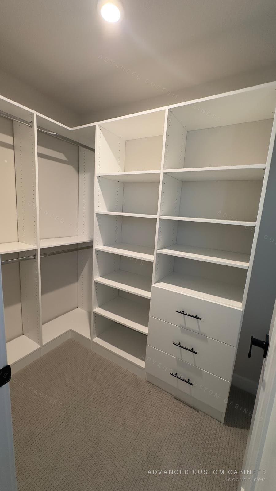 Corner of a white walk-in closet with two open-shelf towers, one over four drawers with black bar pulls, beside double hanging