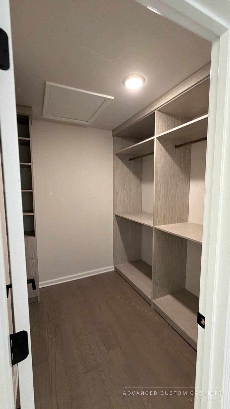 Grey-oak walk-in closet with double hanging and shelving along both walls under a recessed ceiling light