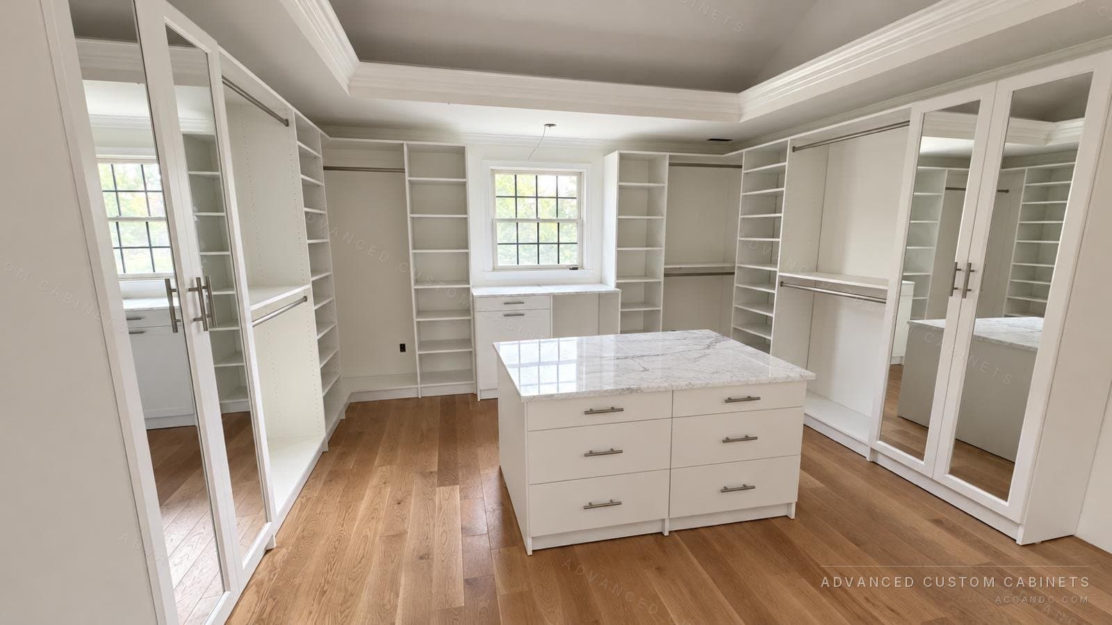 Large white walk-in closet with a marble-top drawer island, mirrored wardrobe doors, open shoe shelving and hanging sections under a tray ceiling